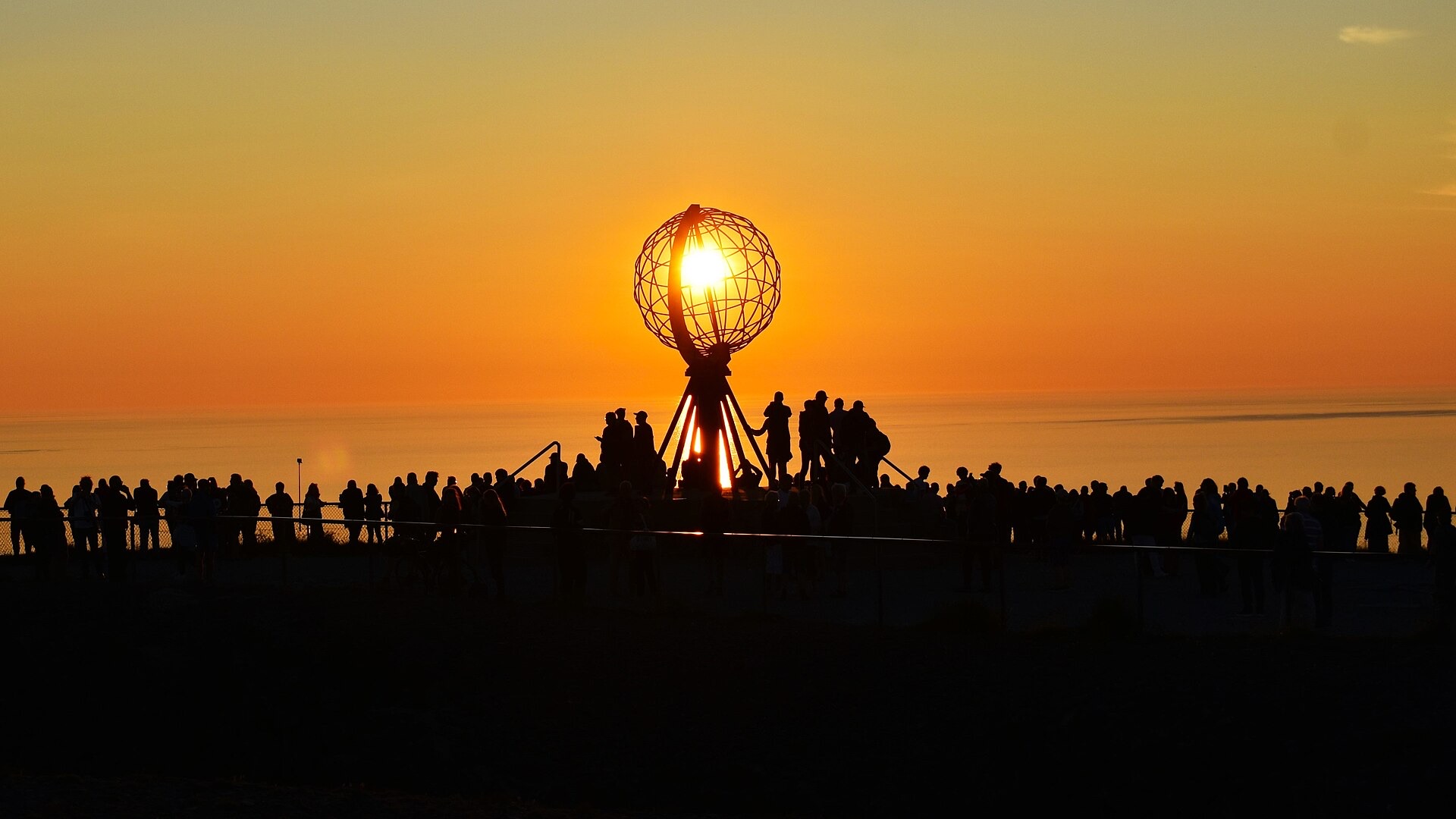 The midnight sun shining through the globe monument above silhouetted visitors at North Cape, Norway