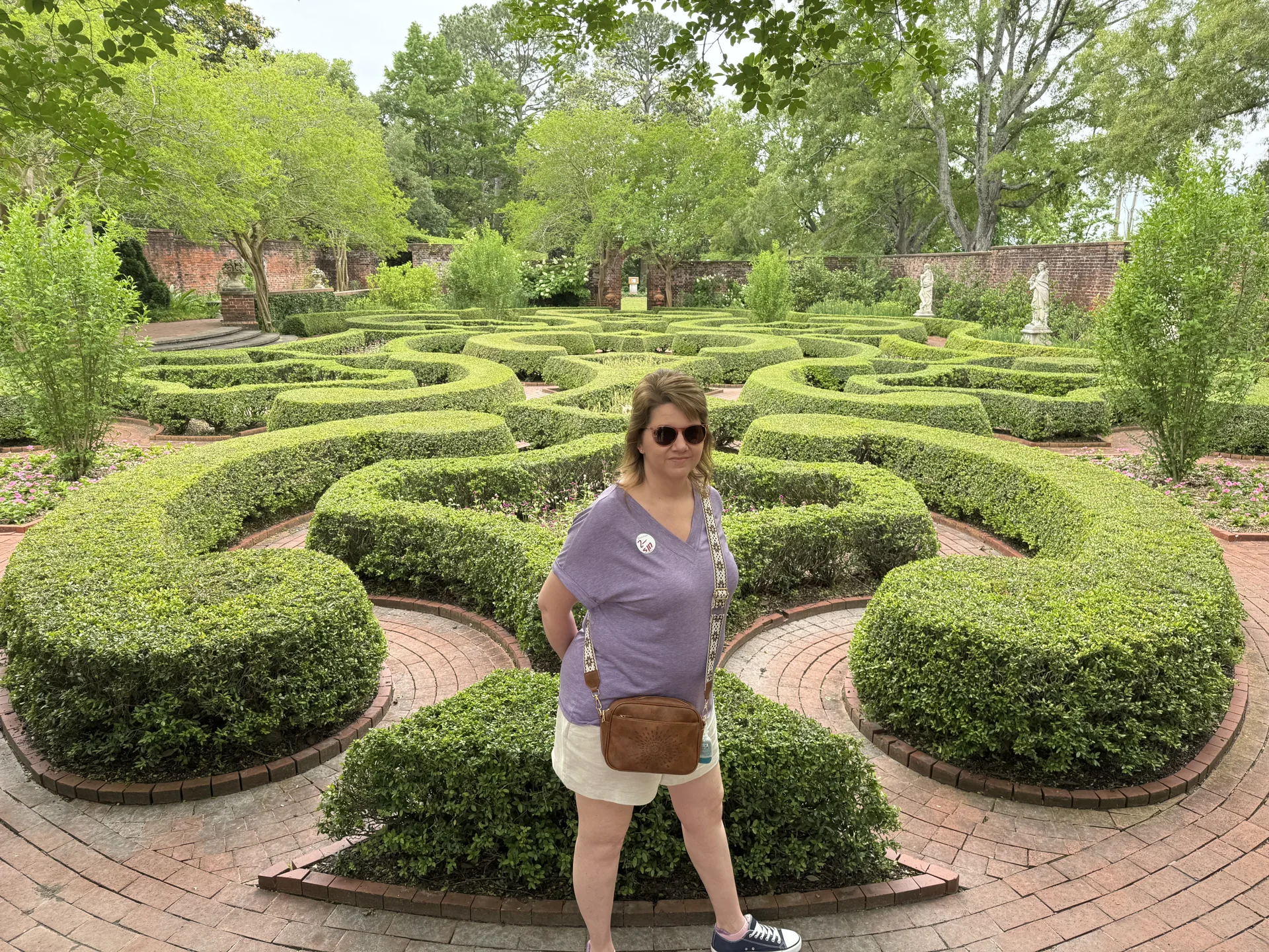 Angela standing beside curving clipped hedges and brick paths in the Tryon Palace gardens
