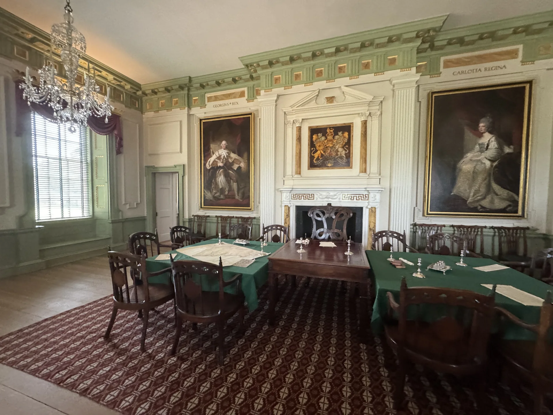 A furnished room at Tryon Palace with green-covered tables, large portraits, and a chandelier