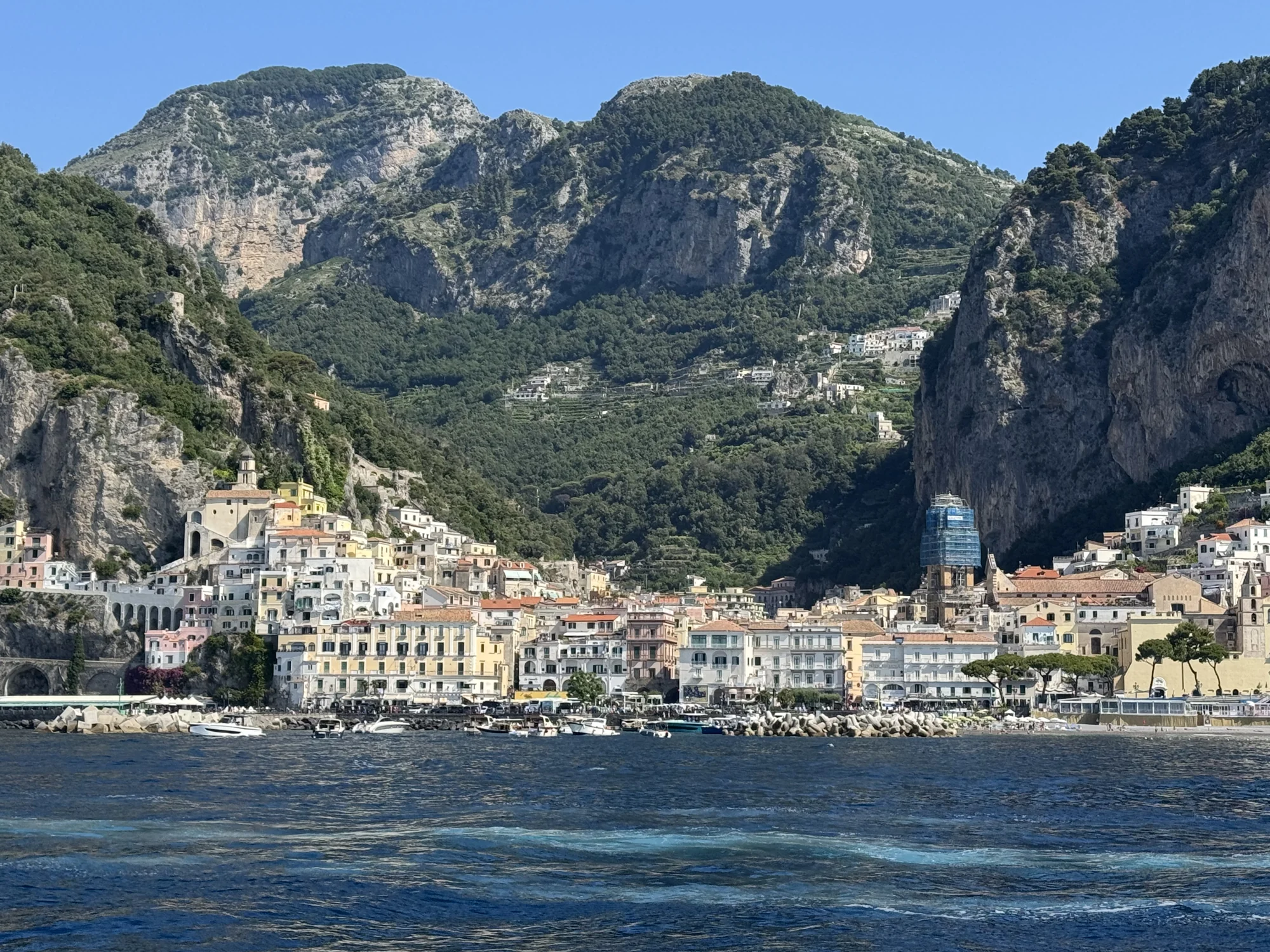 Amalfi’s waterfront buildings below steep green hills, seen from the ferry