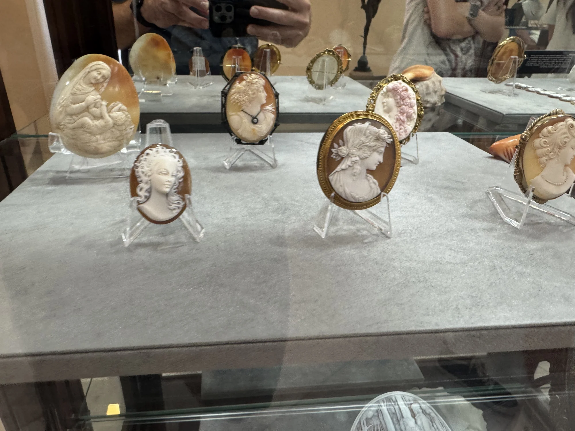Carved shell cameos at Palazzo del Corallo with pale portraits and figures against warm brown backgrounds in a glass display case