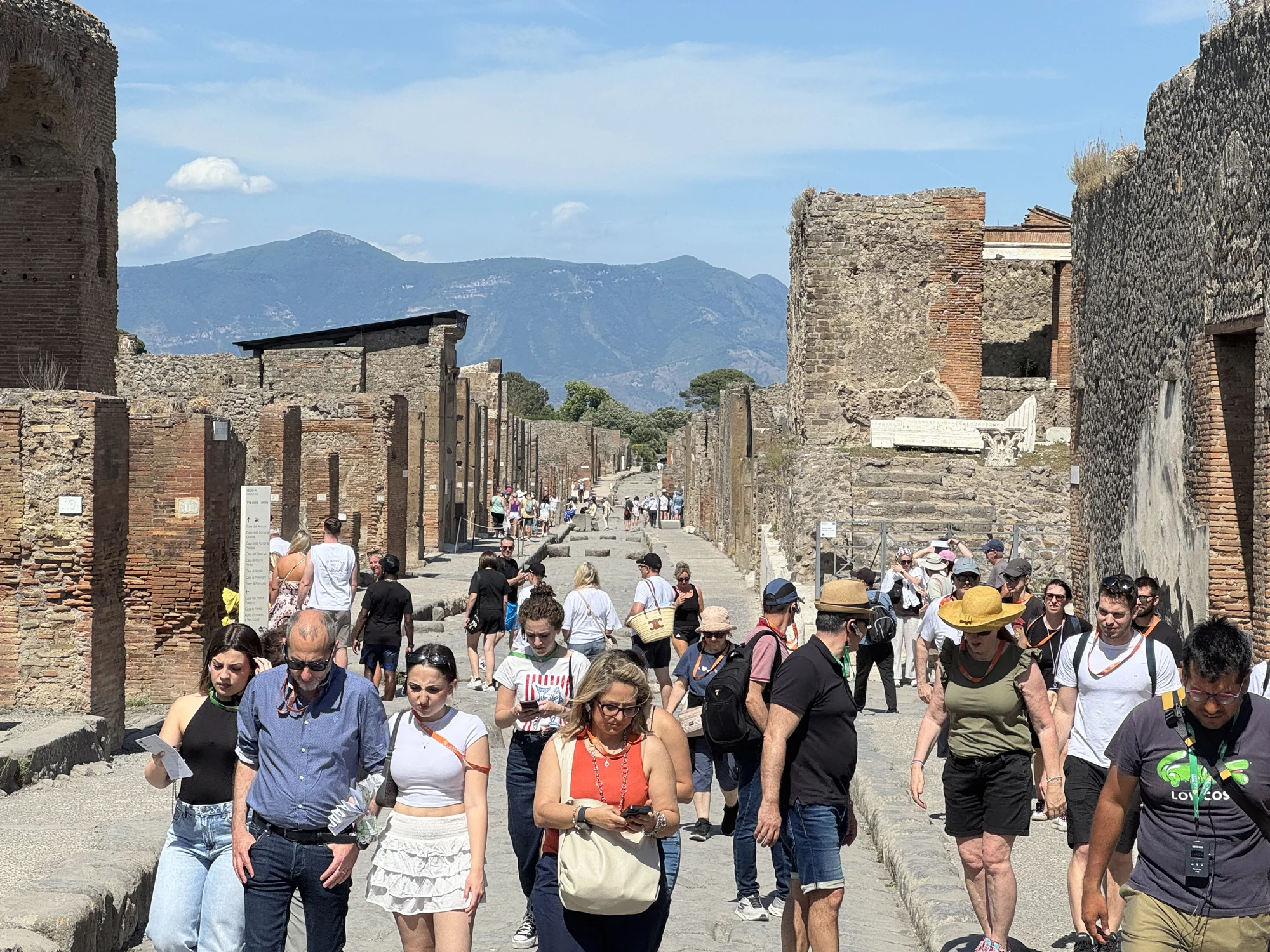 Visitors walking along a stone-paved street between the ruins of Pompeii