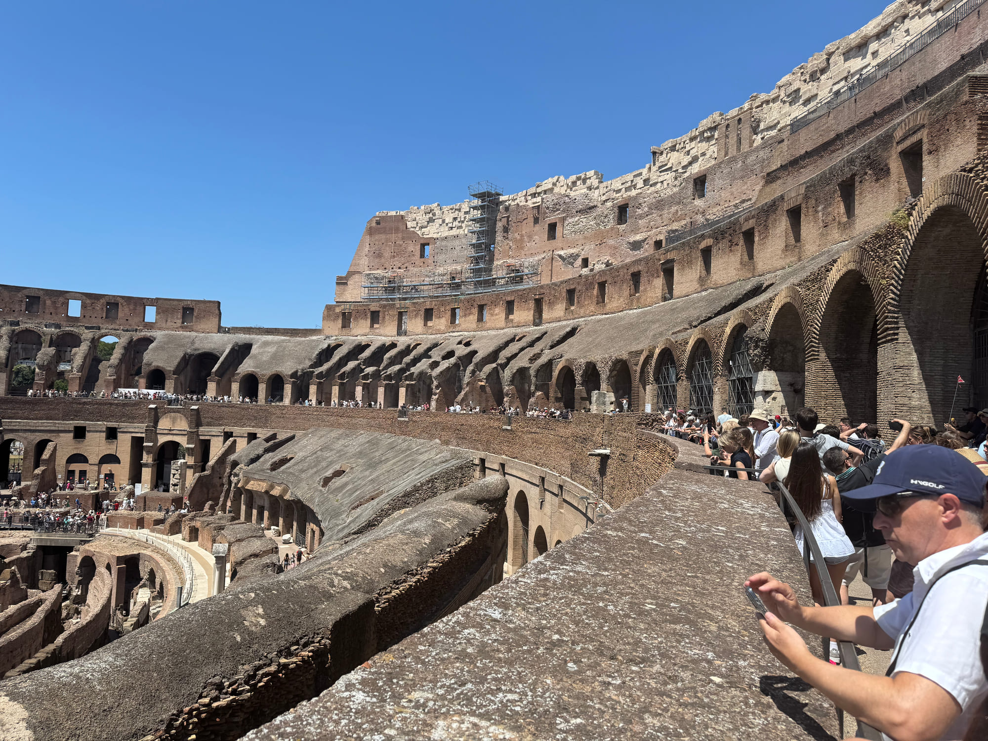 Crowded upper walkway inside the Colosseum overlooking its arches and exposed underground structures