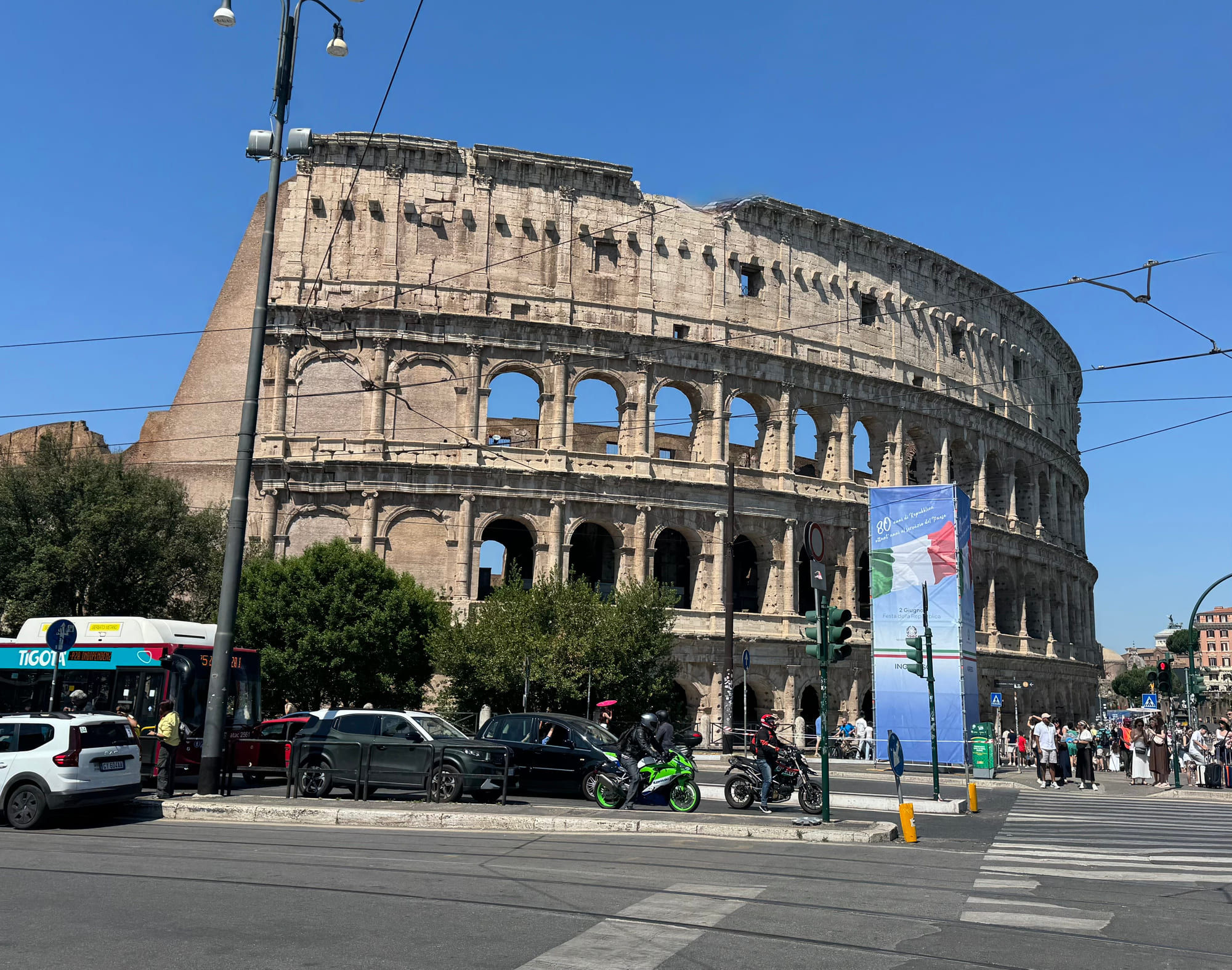 The exterior of the Colosseum beside a busy Rome intersection under a clear blue sky