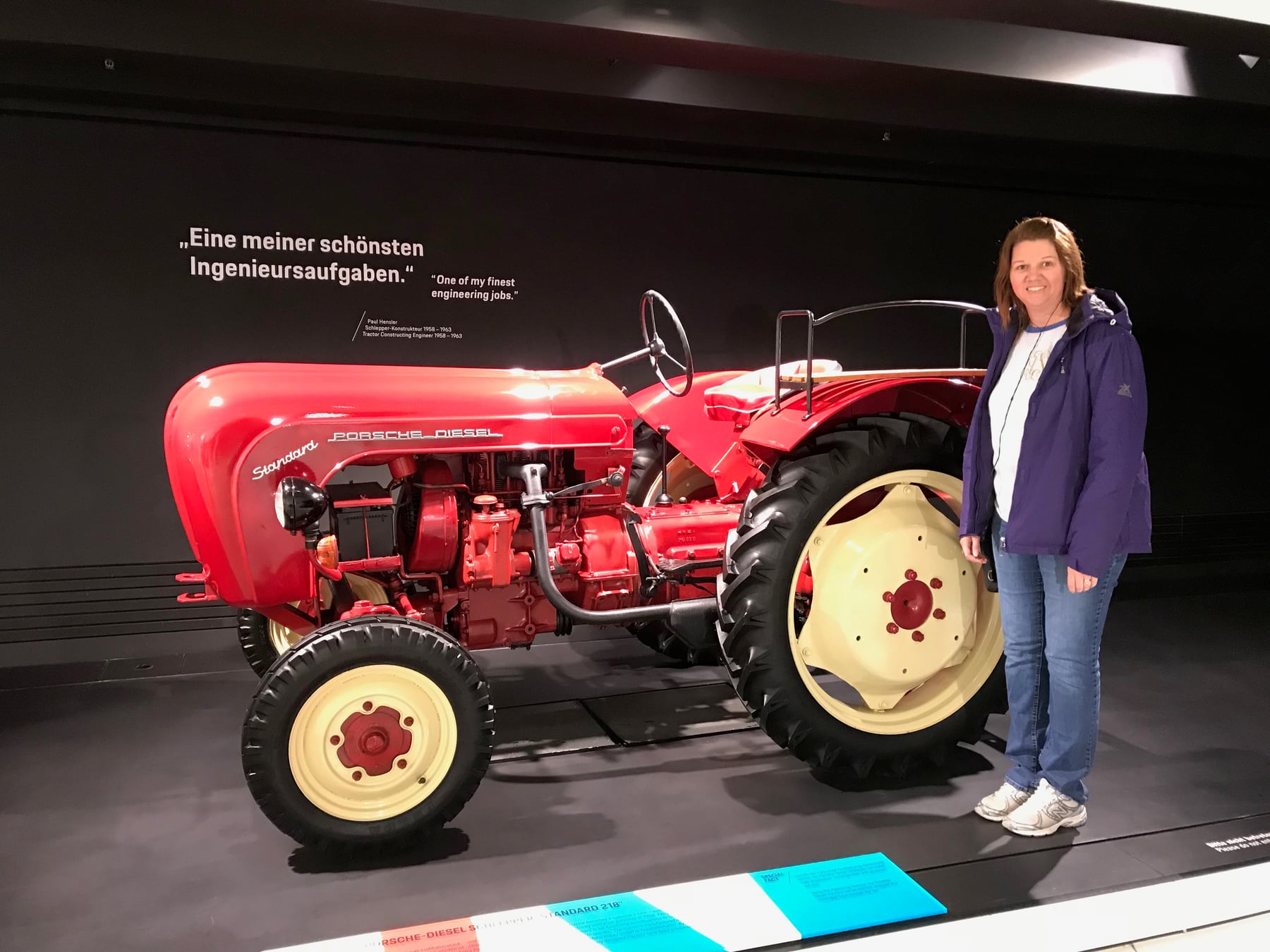 Angela standing beside a red Porsche-Diesel tractor inside the Porsche Museum