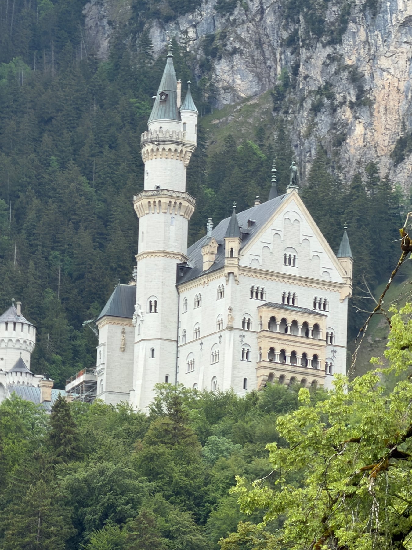 Neuschwanstein Castle rising above green forest beneath a rocky mountainside