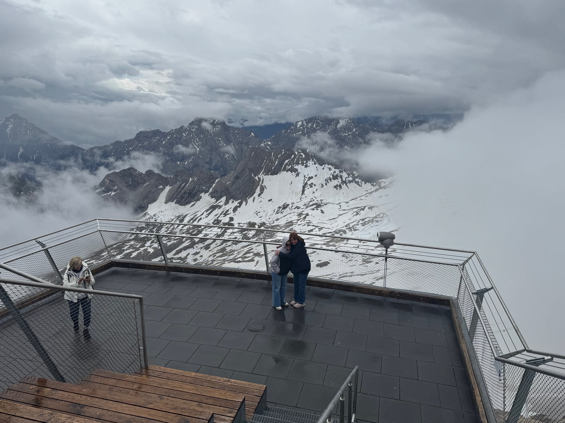 Angela and a family member on the Zugspitze observation terrace with snowy mountains breaking through low clouds