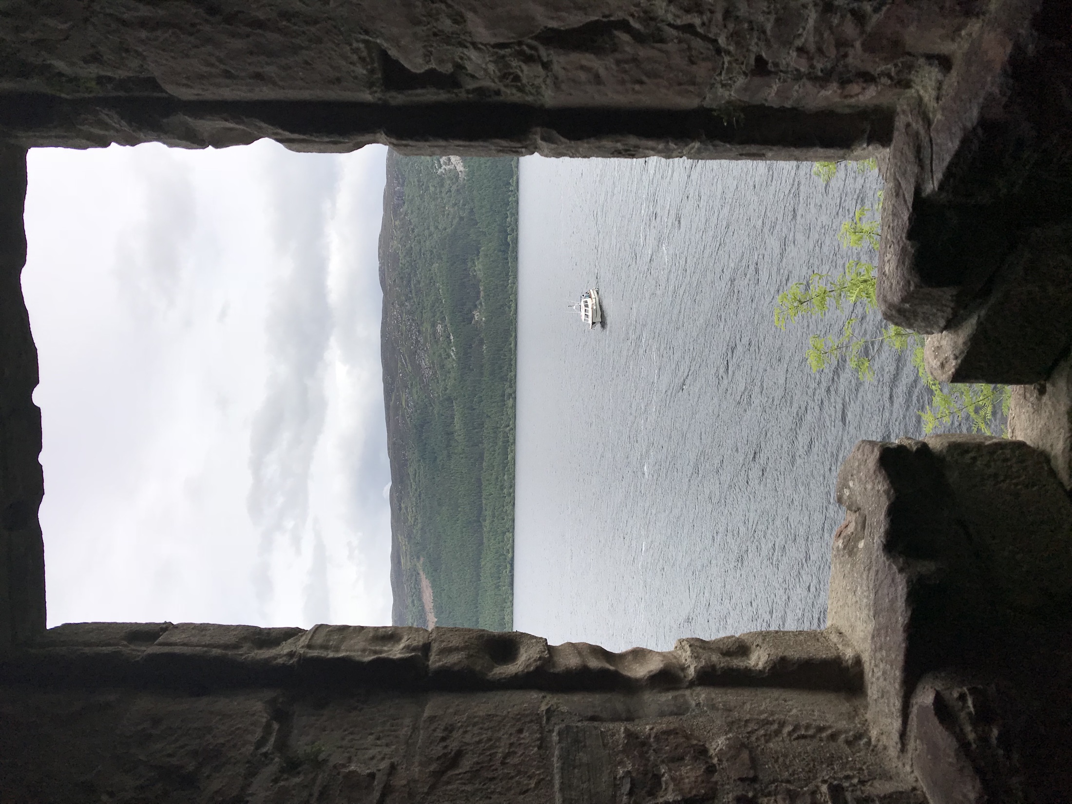 Loch Ness and a small boat framed by a narrow stone window in the castle ruins