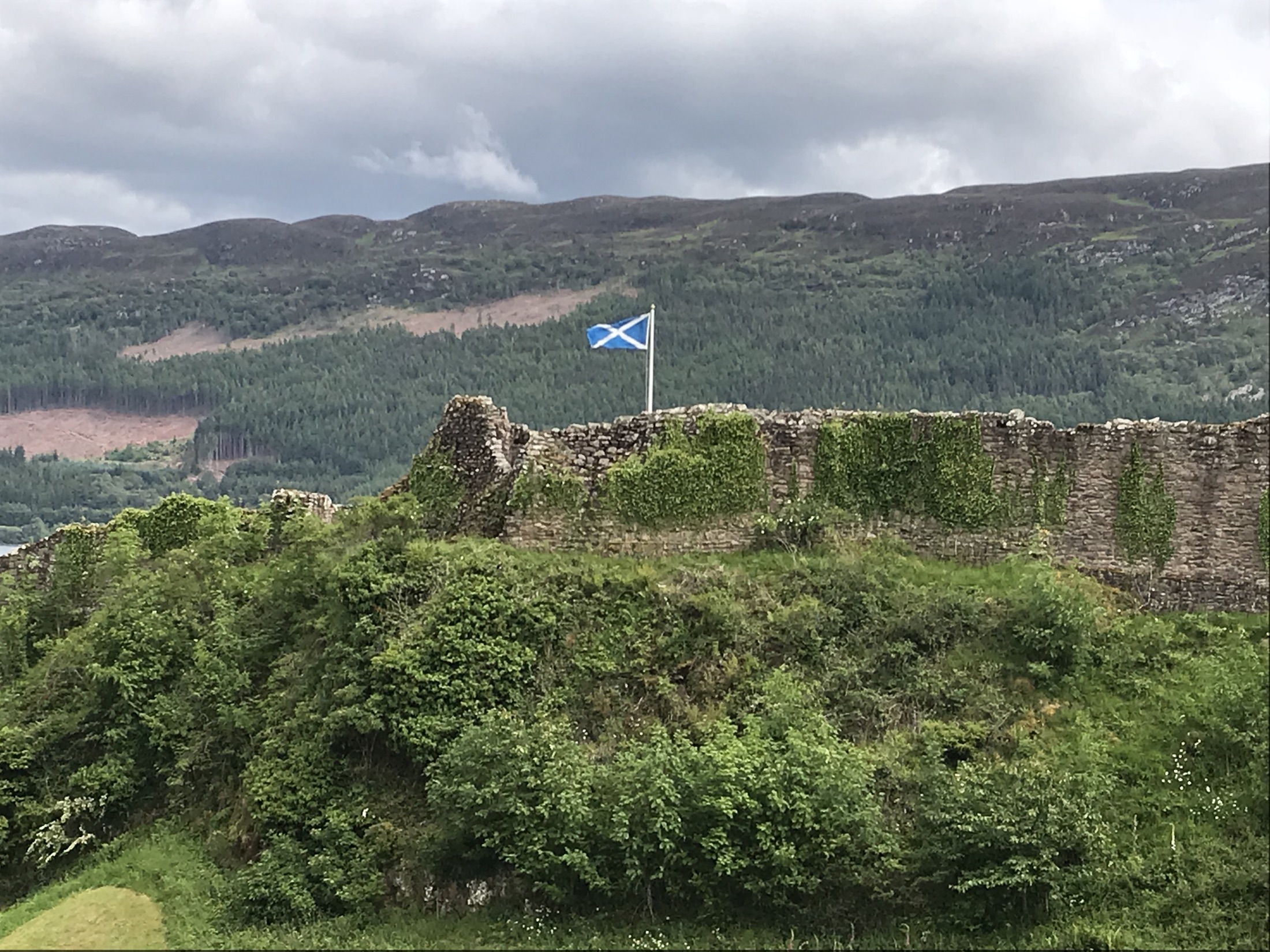 A Scottish flag flying above an ivy-covered stone wall at Urquhart Castle