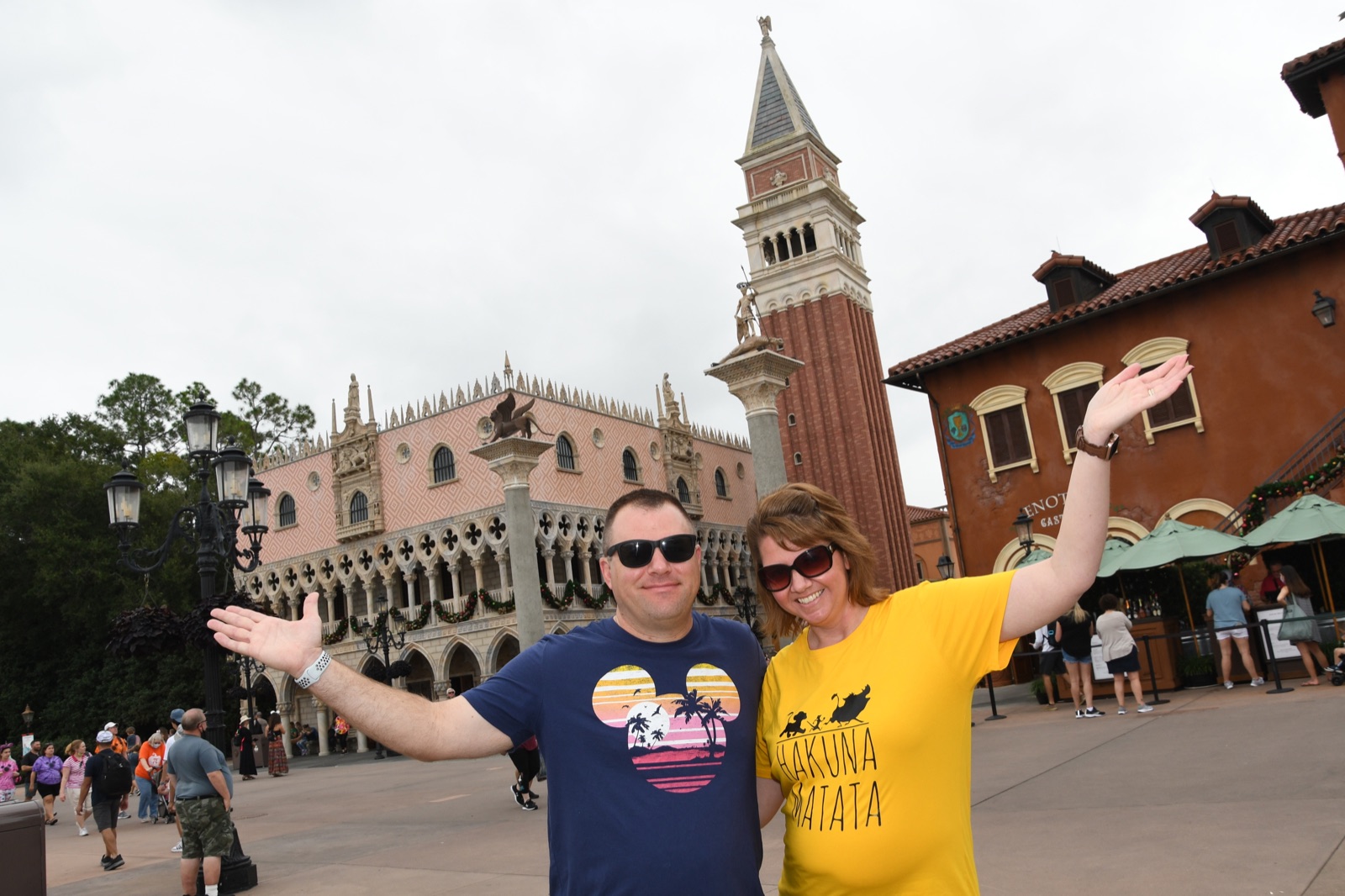 Angela and Brian smiling with their arms open in front of the Italy pavilion at EPCOT