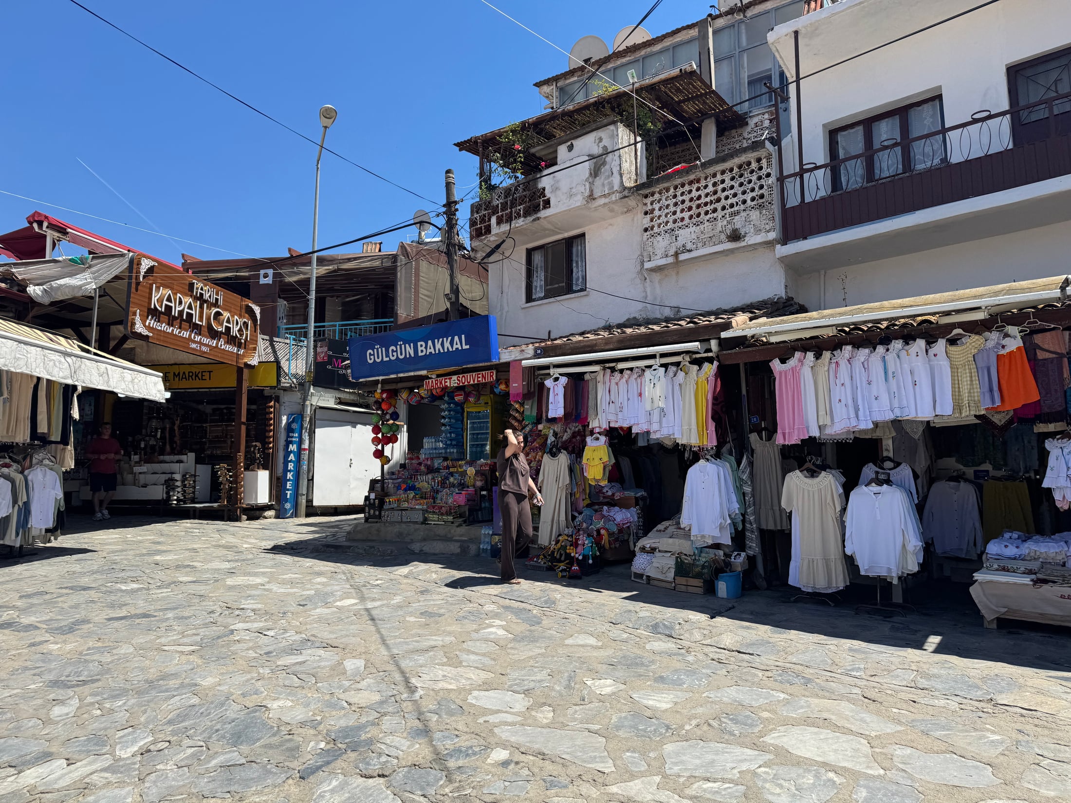 Clothing, local goods, and souvenirs displayed along a stone-paved shopping street in Şirince
