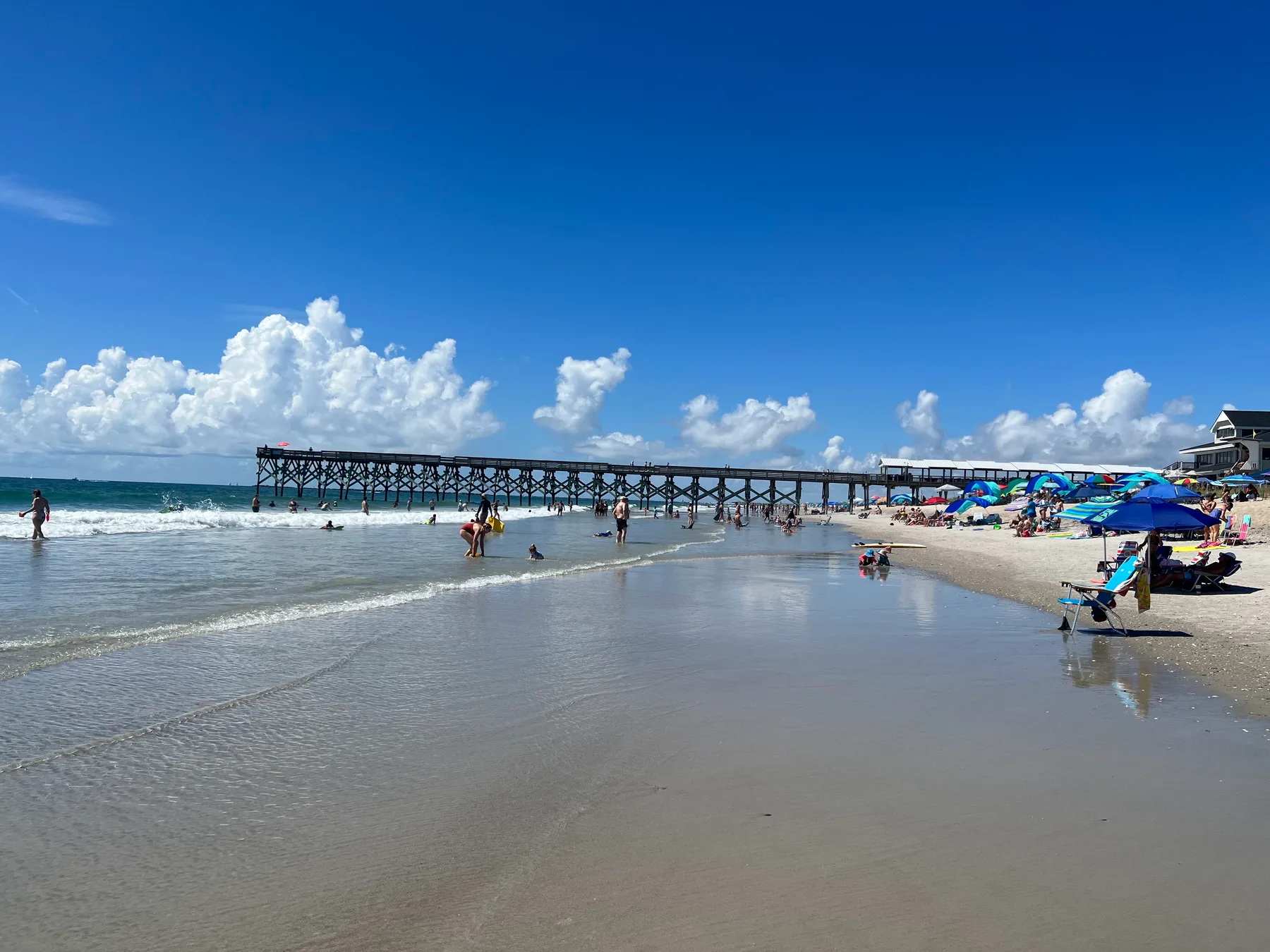 Beachgoers along the Atlantic shoreline beside Crystal Pier at Wrightsville Beach